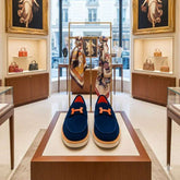 Blue shoes with orange accents on a wooden stand in a high-end store setting.